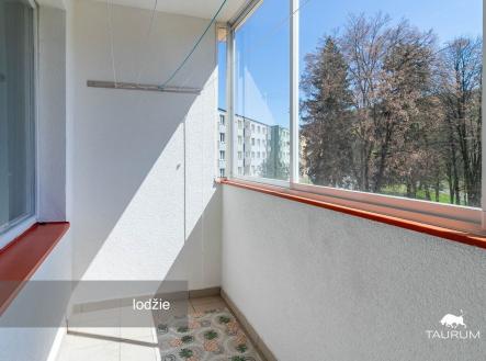Zasklená lodžie v panelovém domě, dlažba na podlaze, výhled na stromy a okolní zástavbu, vhodná pro posezení či sušení prádla.