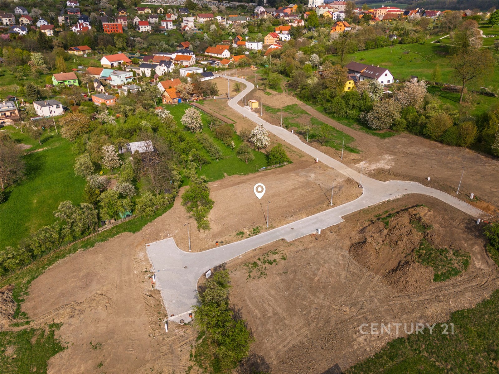 Stavební pozemek s asfaltovou příjezdovou cestou, obklopený zelení a klidnou lokalitou, ideální pro rodinný dům nebo investici.