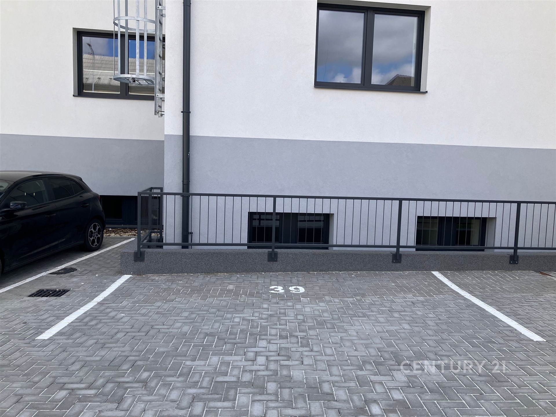 Prázdné parkovací místo s dlažbou, označené číslem 39, vedle moderní budovy. Vhodné pro parkování rezidentů v městské oblasti.