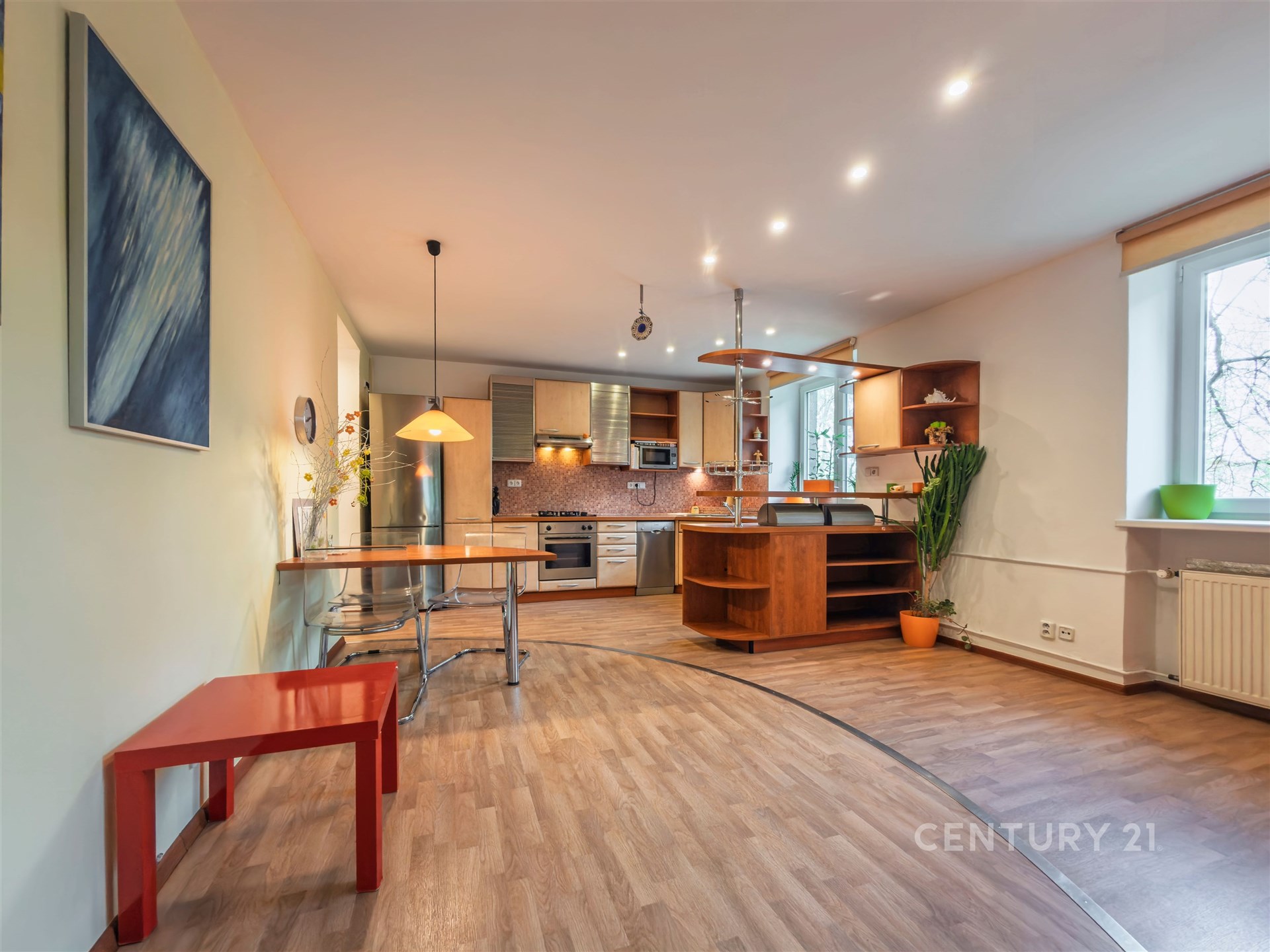 Moderní kuchyň s parketovou podlahou, vestavěnými spotřebiči a velkým oknem umožňujícím dostatek přirozeného světla.