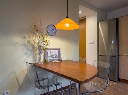 Jídelní kout s moderním dřevěným stolem, parketovou podlahou a designovým osvětlením. Elegantní kombinace skla a dřeva vytváří útulnou atmosféru.