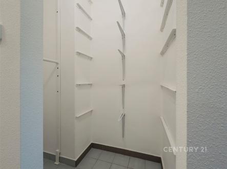 Úložný prostor se světlými stěnami a dlažbou na podlaze, vybavený regálovými policemi. Ideální pro uskladnění v moderním bytě.