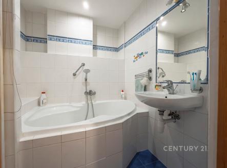 Koupelna s rohovou vanou, modrou dlažbou a bílými obklady, moderní svítidla, prostorná a světlá.