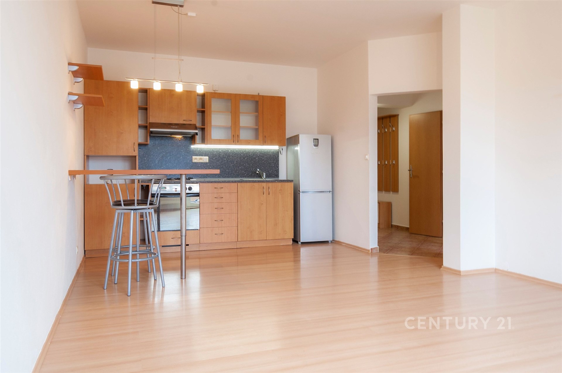 Moderní kuchyň s dřevěnými skříňkami, parketovou podlahou a vestavěnými spotřebiči. Světlý otevřený prostor s moderním designem.