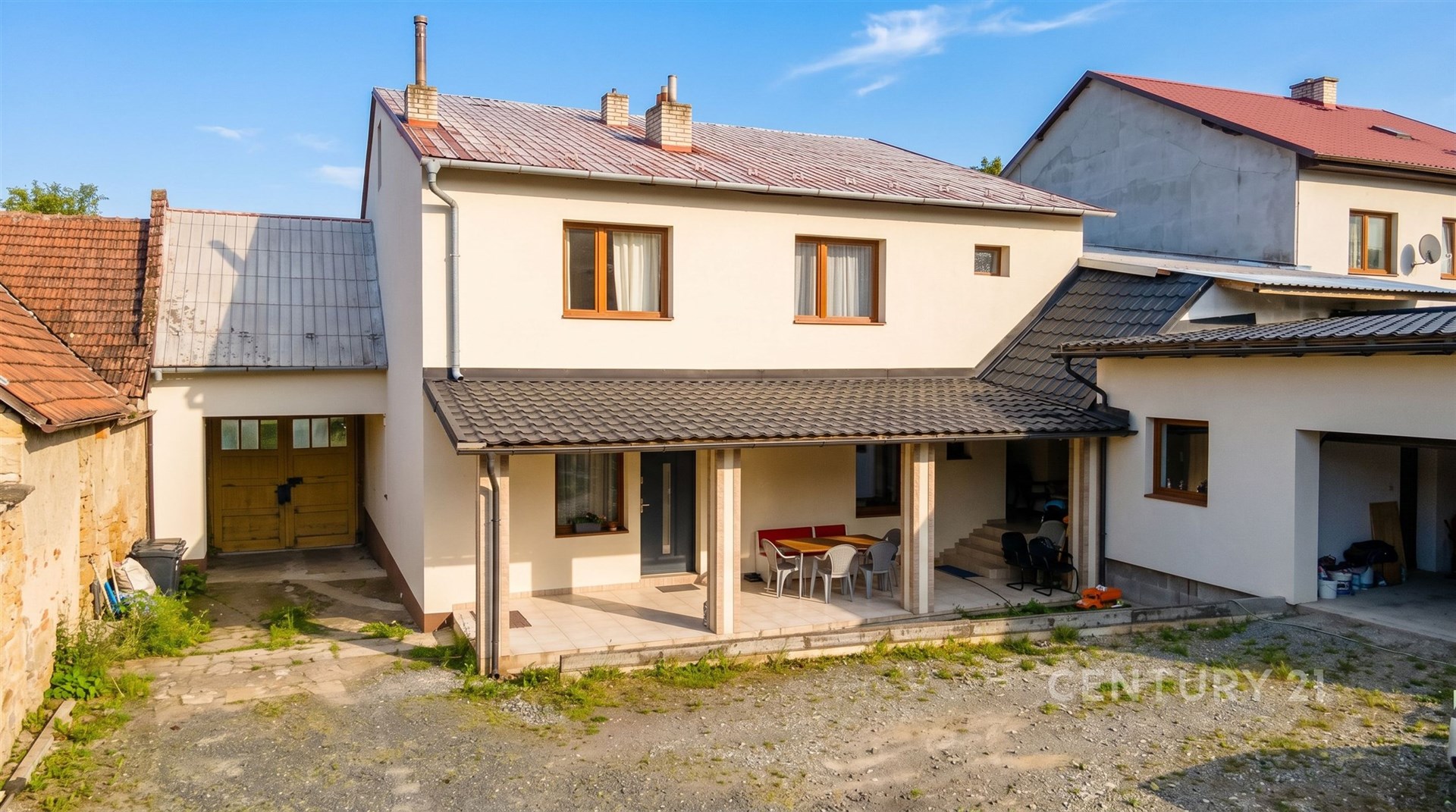 Rodinný dům s terasou, moderní bílé fasády a dřevěnými okny, prostorný dvorek s garáží, klidná lokalita vhodná pro rodinné bydlení.