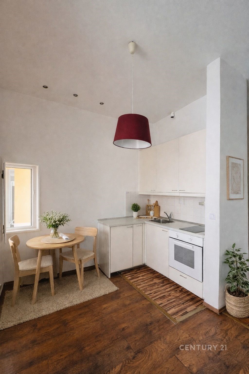 Kompaktní kuchyň s dřevěnou podlahou, moderní bílou linkou a vestavěnými spotřebiči, světlý interiér s jídelním koutem a dekorací.