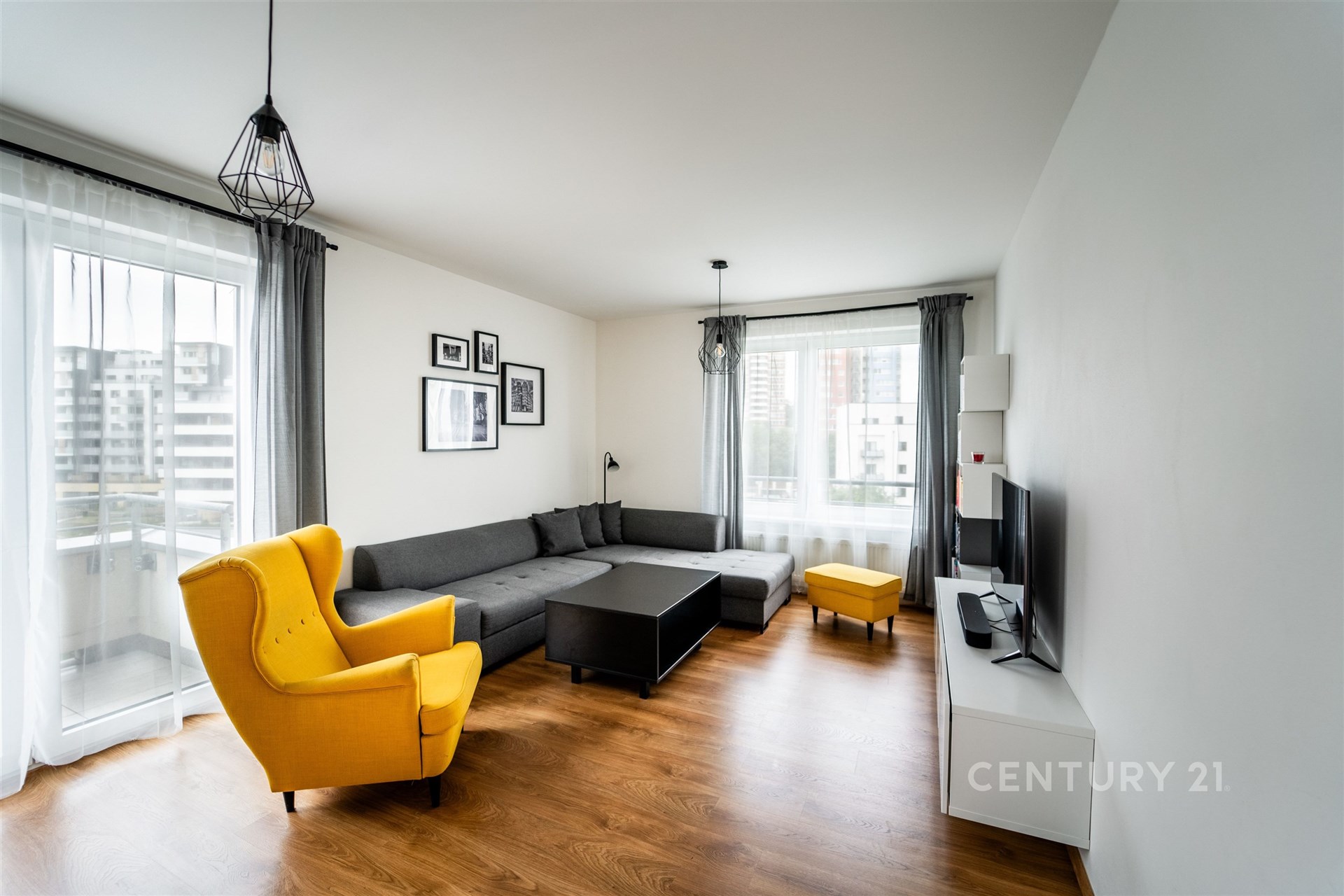 Světlý obývací pokoj s parketovou podlahou, velká okna, moderní design, pohodlná sedací souprava, žluté křeslo pro kontrast.