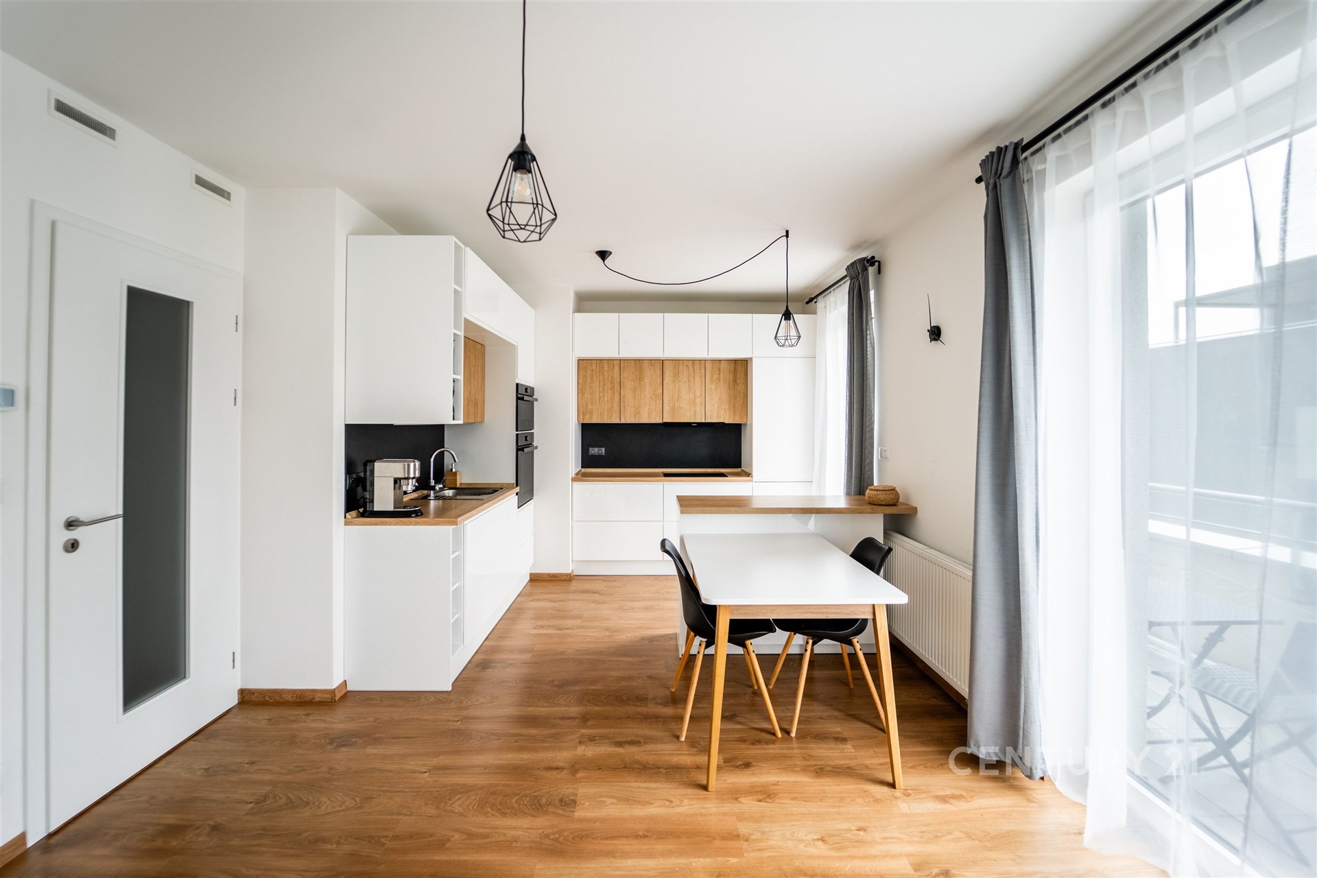 Moderní kuchyň s parketovou podlahou, světlými stěnami a velkými okny. Stylový nábytek a moderní osvětlení dodávají prostoru elegantní atmosféru.
