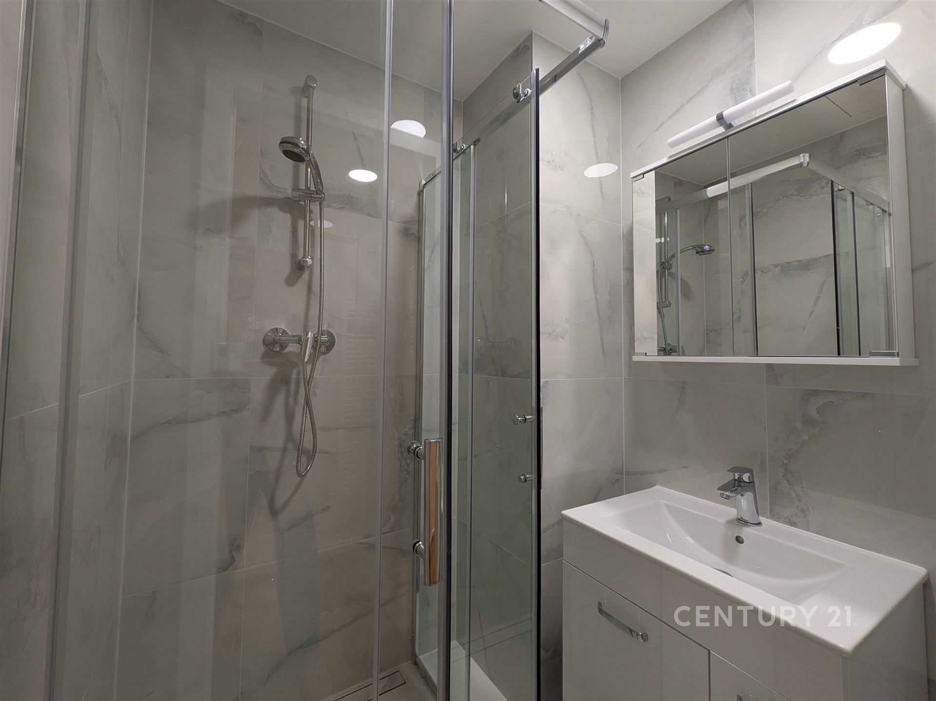 Moderní koupelna s proskleným sprchovým koutem, světlými dlažbami a elegantním umyvadlem, ideální pro moderní bydlení.