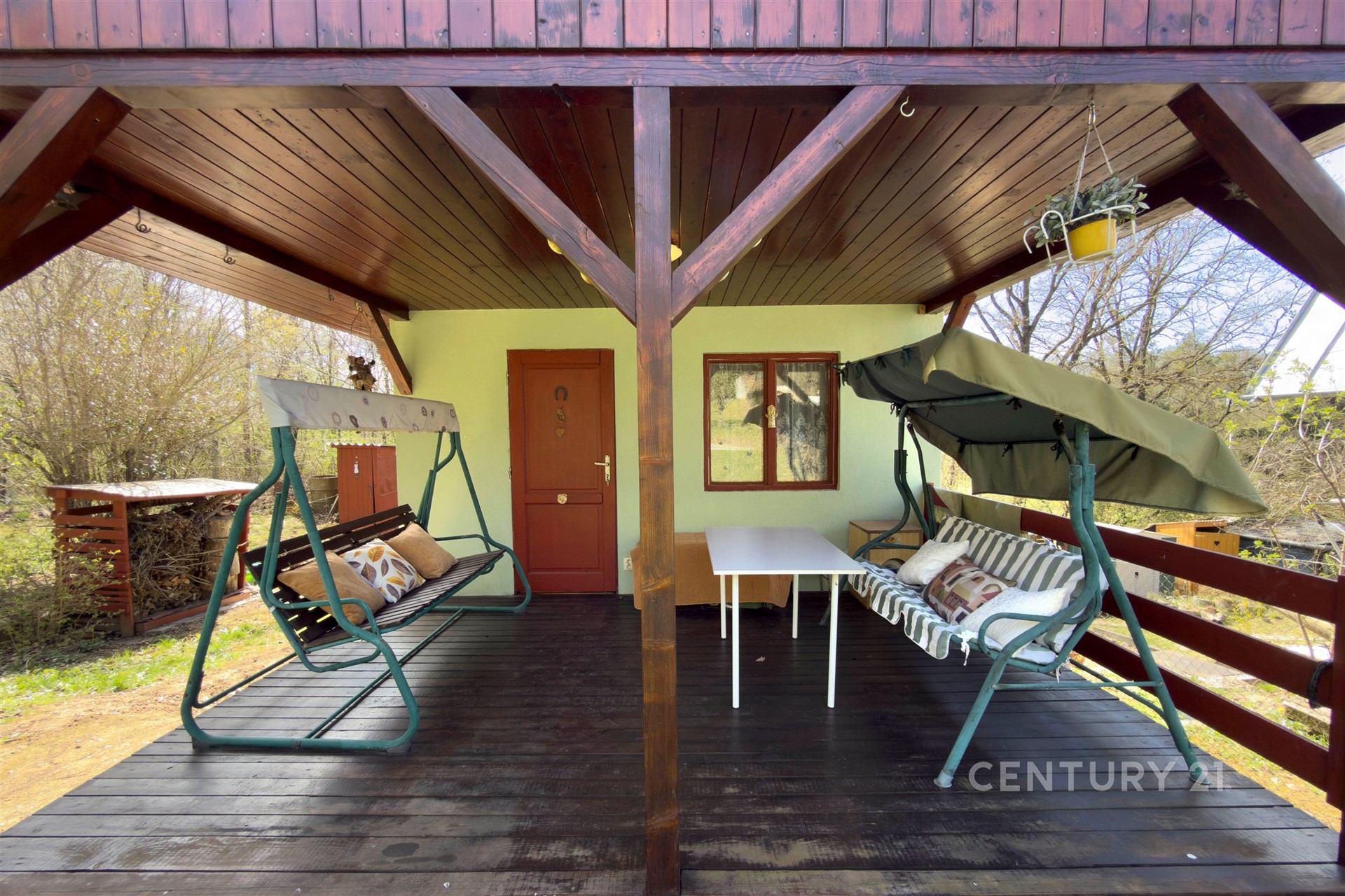 Zastřešená terasa s dřevěnou podlahou a zahradním nábytkem nabízí relaxační prostor, ideální pro venkovní posezení a odpočinek v přírodě.