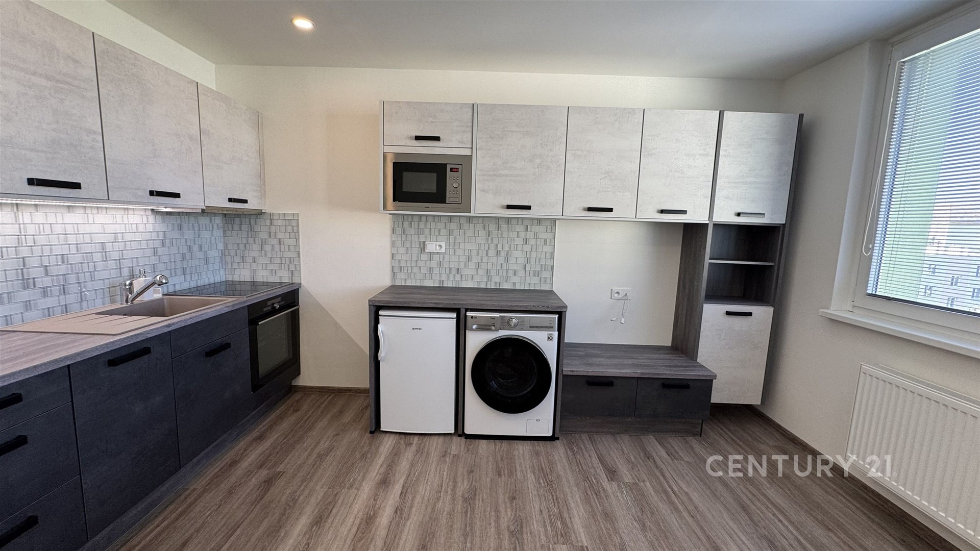 Moderní kuchyň s parketovou podlahou, vestavěné spotřebiče a velká okna poskytují světlý prostor pro vaření i praní prádla.