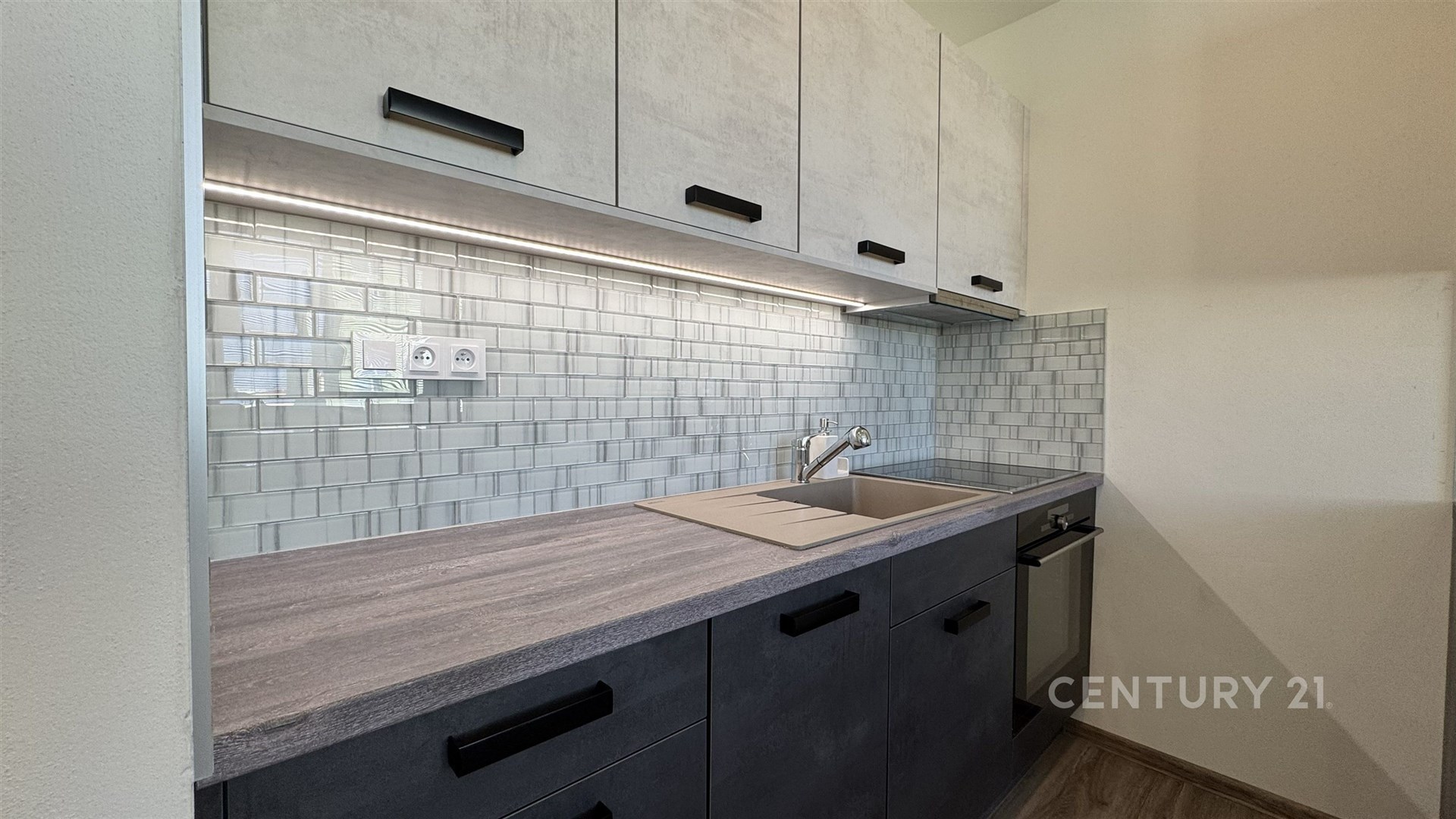 Moderní kuchyň s dlažbou, elegantními skříněmi a vestavěnou troubou, která nabízí stylové a funkční uspořádání pro každodenní vaření.