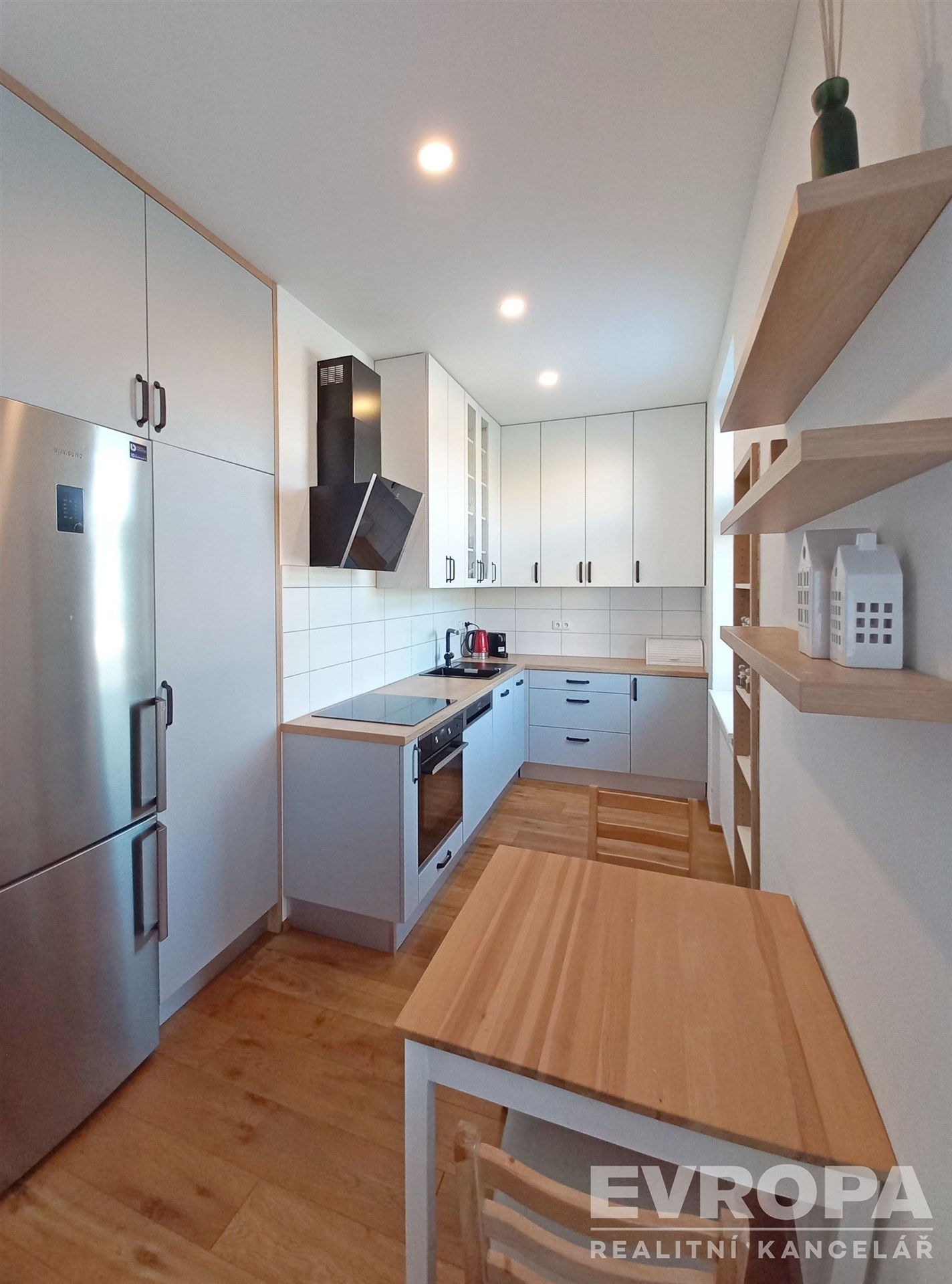 Moderní kuchyň s vestavěnými spotřebiči, dřevěné podlahy a světlé skříňky, útulný prostor pro pohodlné vaření a stolování.