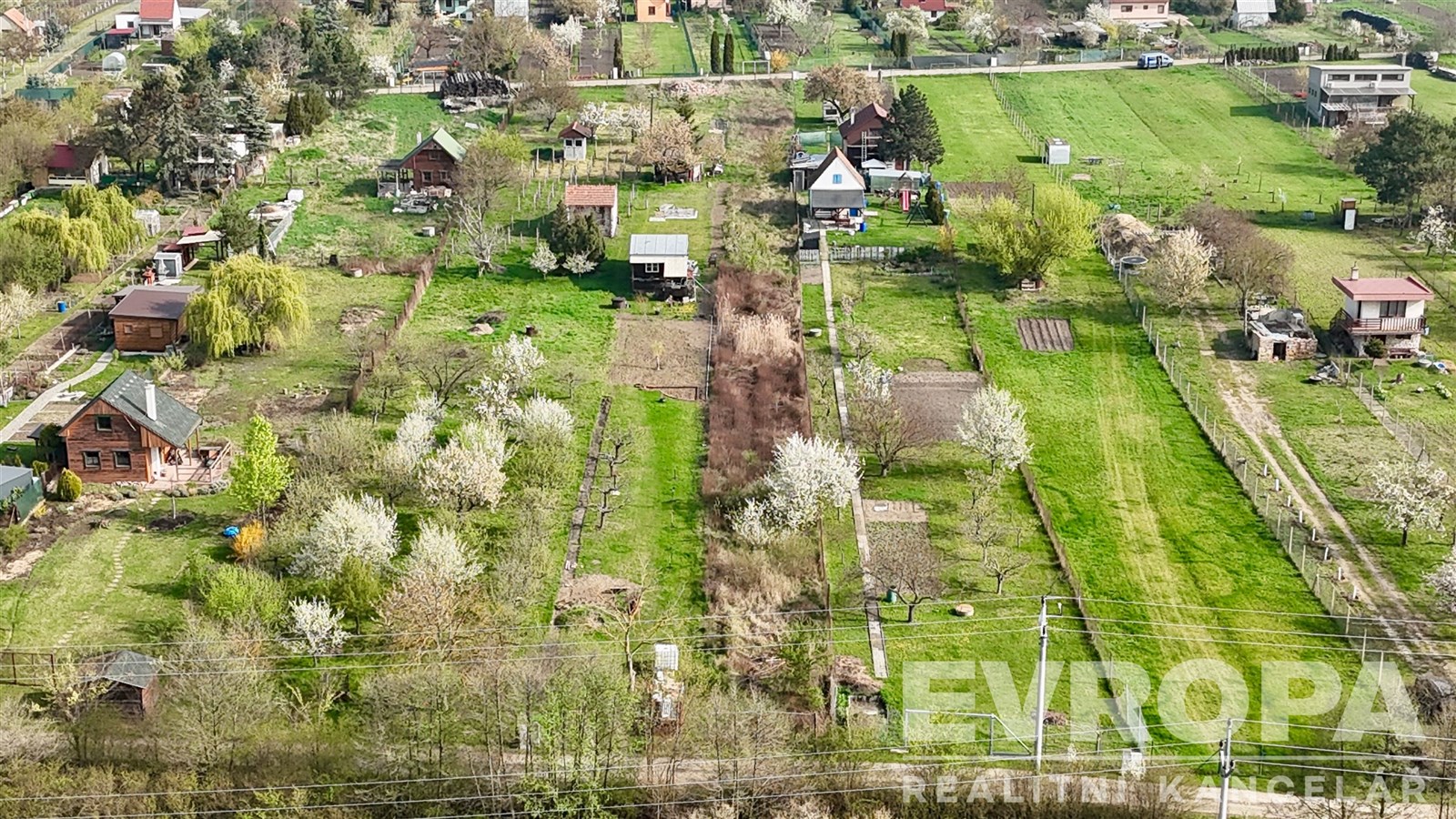 Pohled na rozlehlé zahrady s kvetoucími stromy, chatkami a zelenými trávníky. Klidná lokalita nabízí soukromí a prostor pro zahradničení.