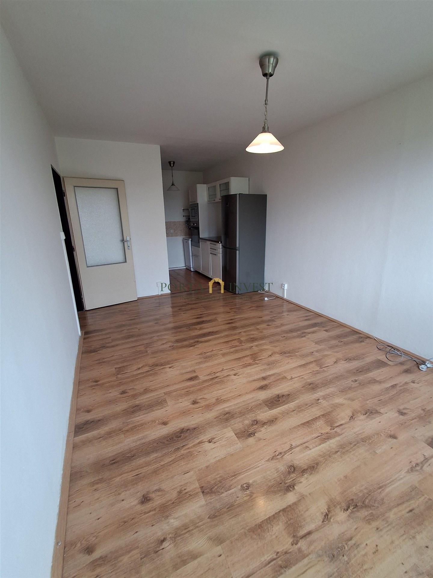 Jídelní kout s moderní dřevěnou podlahou, prostorný interiér a světlé stěny, plně vybavená kuchyň s lednicí a závěsnými svítidly.