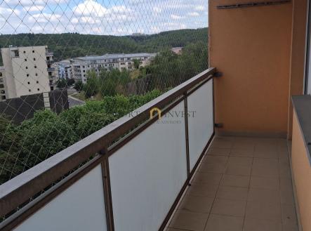 Prostorný balkon s dlažbou a bezpečnostní sítí, výhled na okolní zeleň a městskou krajinu, ideální pro odpočinek