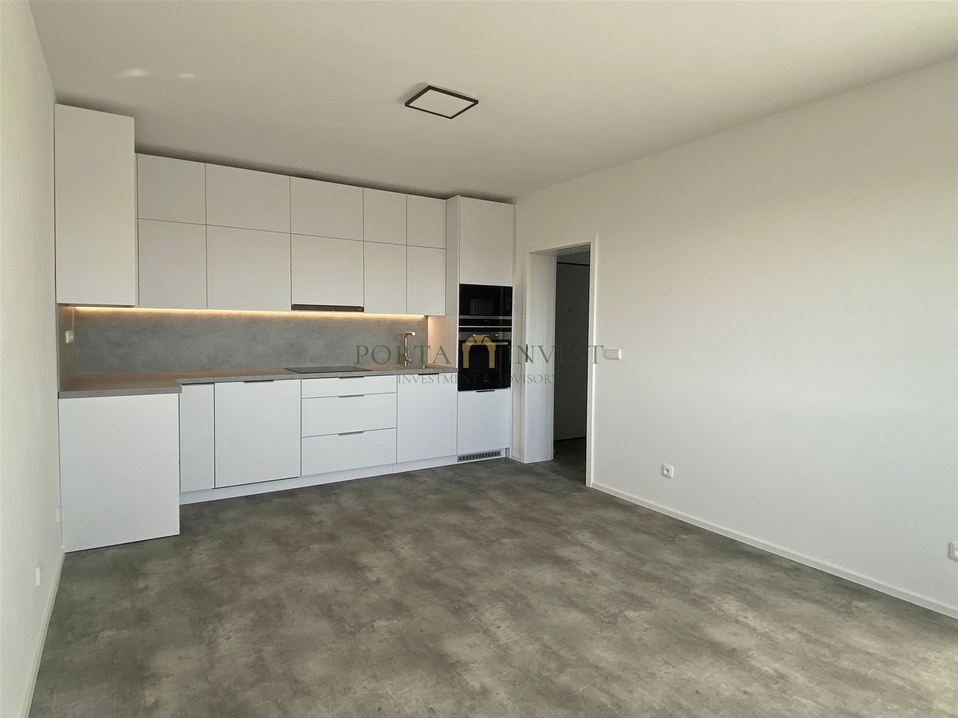 Moderní kuchyň s vestavěnými skříněmi, dlažba v šedém odstínu, minimalistický design, světlé stěny a elegantní osvětlení.