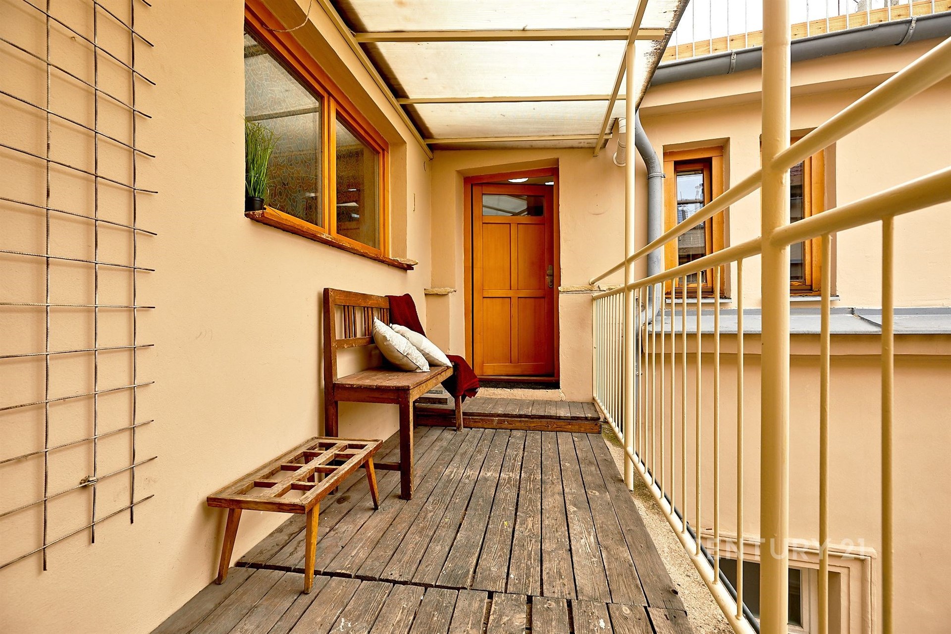 Zrekonstruovaný balkon s dřevěnou podlahou, minimalistickým dřevěným nábytkem a velkými okny, poskytujícími dostatek přirozeného světla.