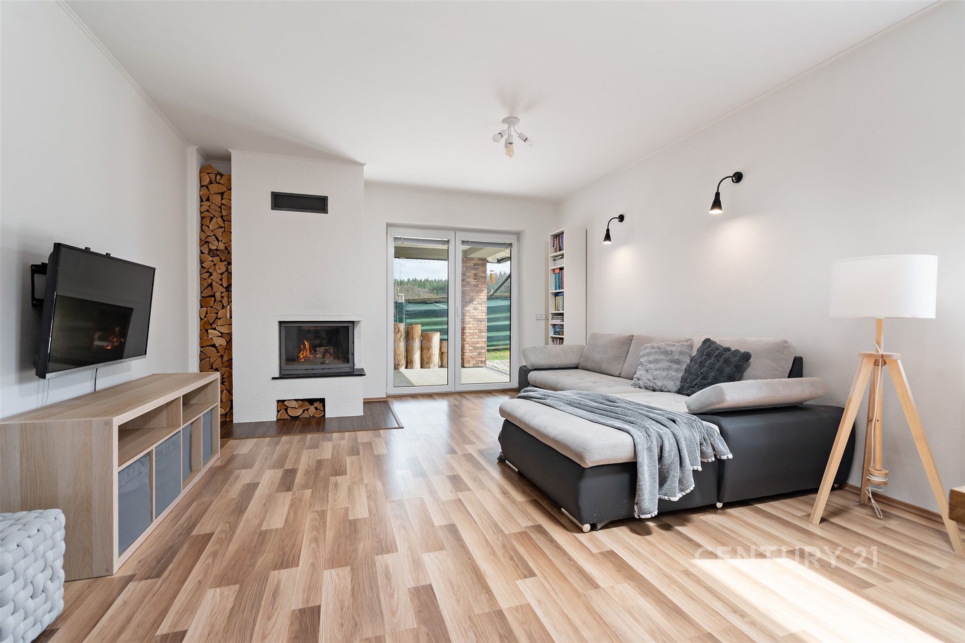 Světlý obývací pokoj s parketovou podlahou, moderní krbová kamna a velká okna, které zajišťují dostatek přirozeného světla
