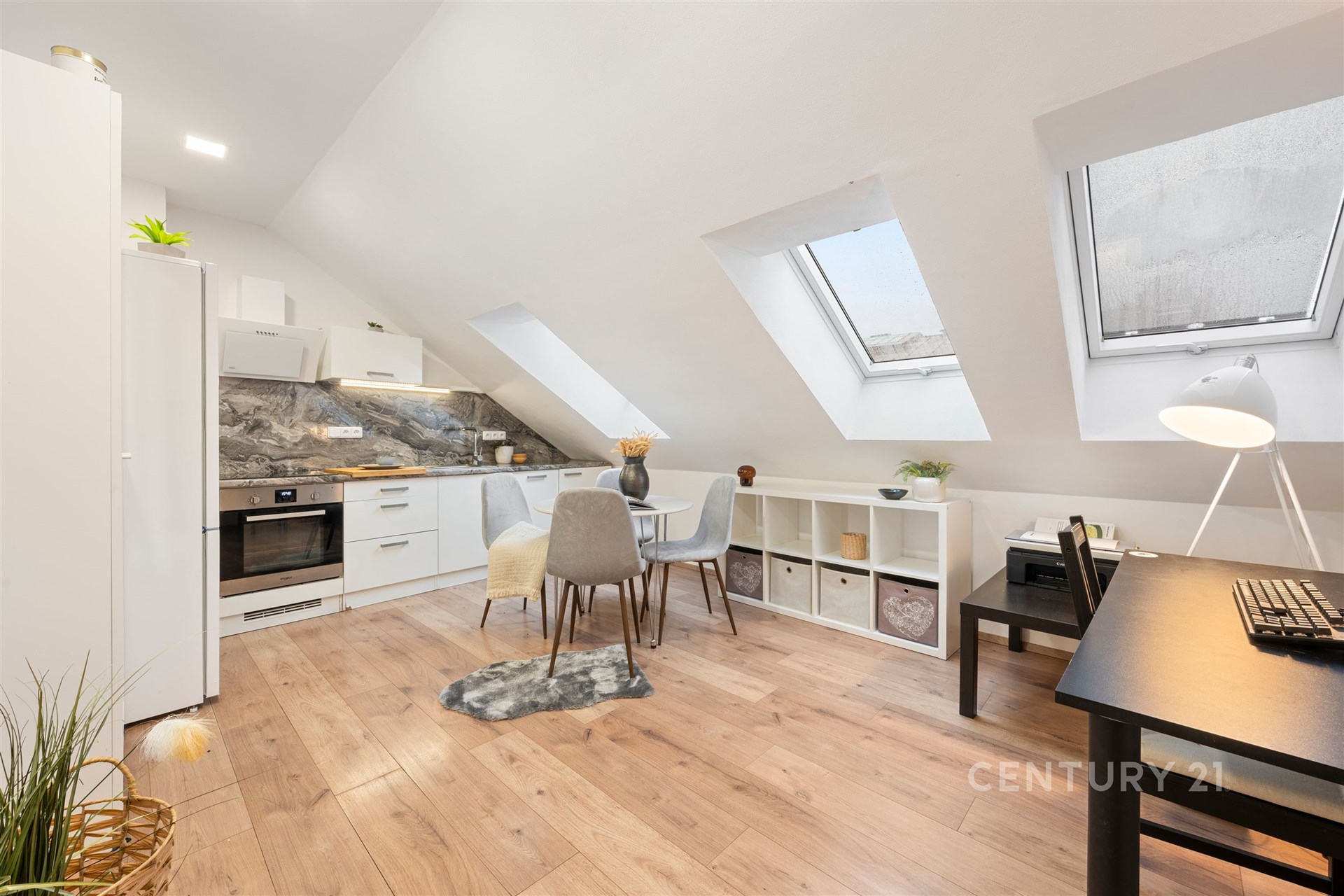 Podkrovní kuchyň a jídelna s moderními spotřebiči, dřevěnou podlahou a velkými střešními okny, vytvářející světlý prostor.