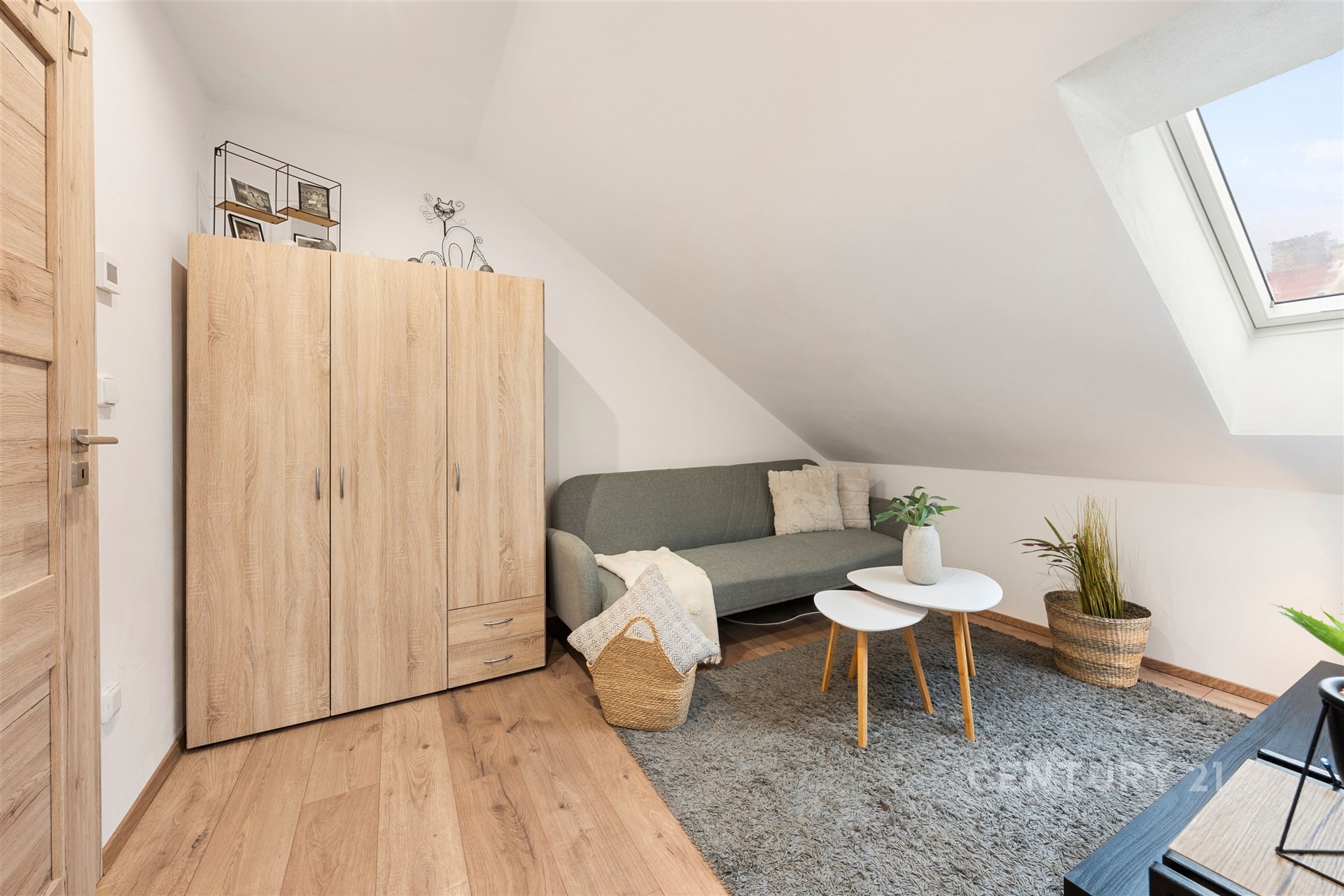 Podkrovní obývací pokoj s parketovou podlahou, střešními okny a moderním nábytkem, poskytující útulný a světlý prostor pro relaxaci.