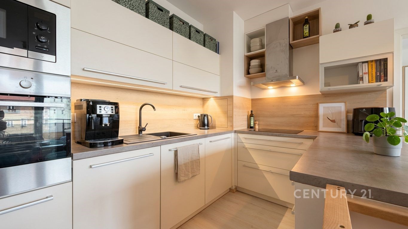 Moderní kuchyň s vestavěnými spotřebiči, světlou dřevěnou linkou a parketovou podlahou, ideální pro stylové bydlení.