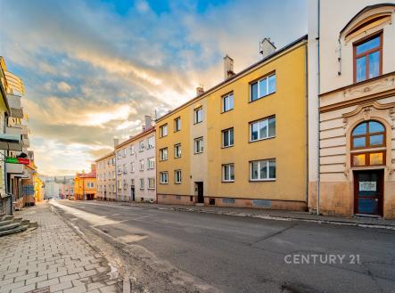 Vícepatrový městský dům s tradiční fasádou, velká okna, asfaltová cesta, blízkost centra, slunečné podvečerní osvětlení