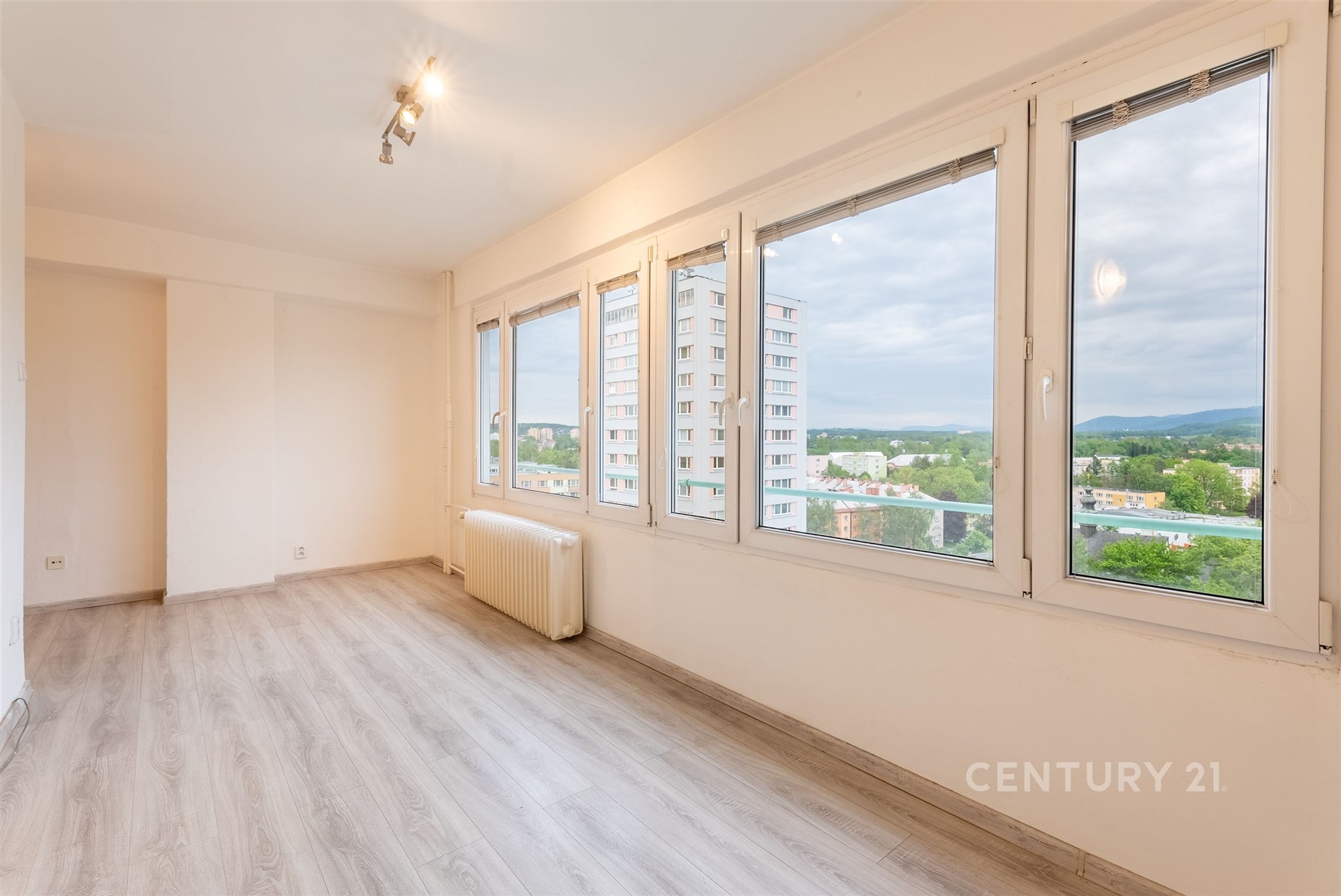 Světlý obývací pokoj s velkými okny, moderní laminátovou podlahou a výhledem na okolí, nabízí prostorný a útulný interiér.