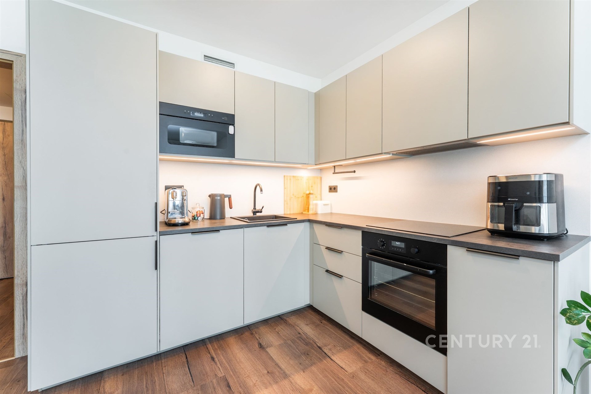 Moderní kuchyň s vestavěnými spotřebiči, parketová podlaha, světlé skříňky a dřevěné detaily, elegantní a funkční design.