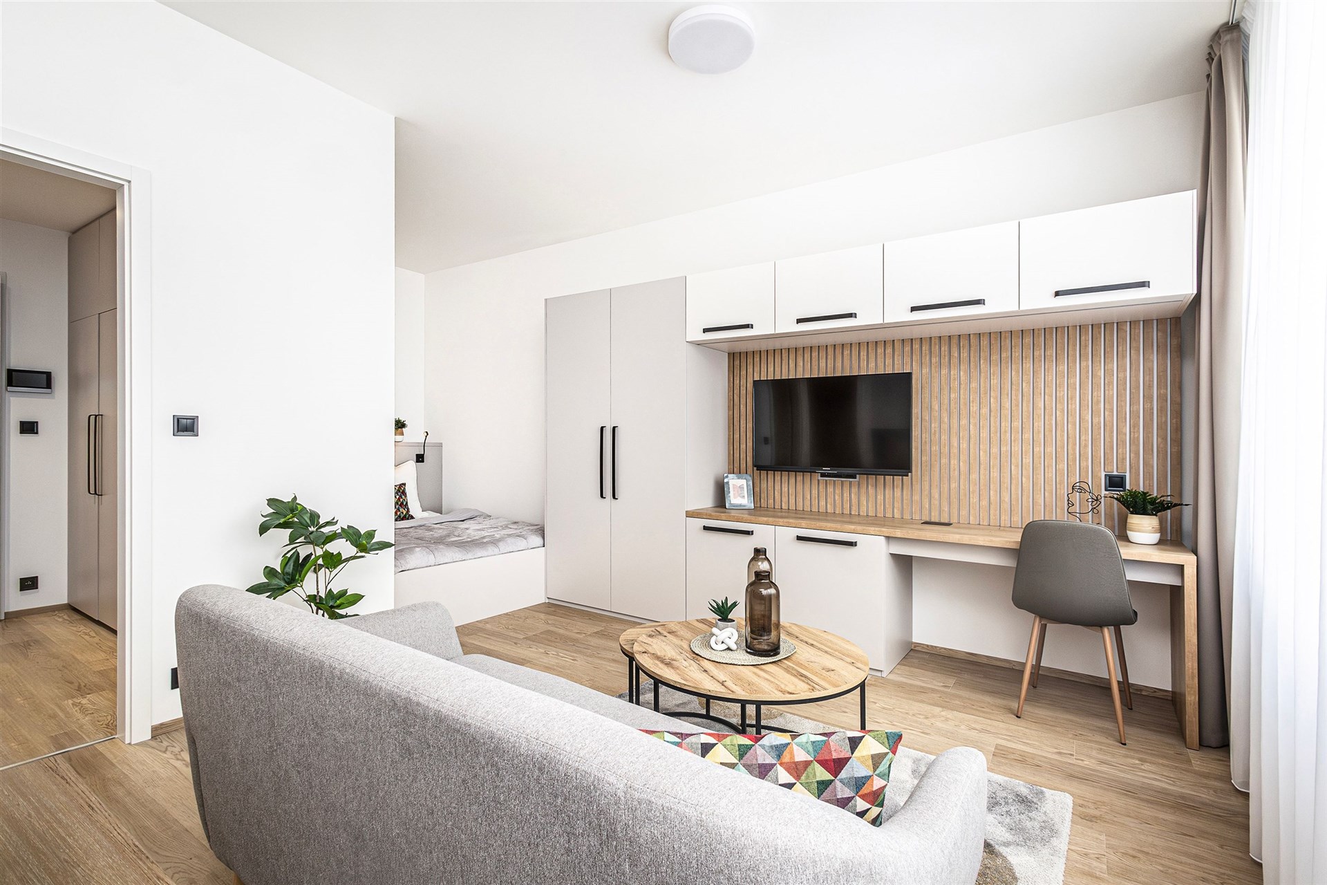 Světlý obývací pokoj s parketovou podlahou, vestavěné skříně, moderní nábytek, velká okna, minimalistický design, pohodlné posezení.