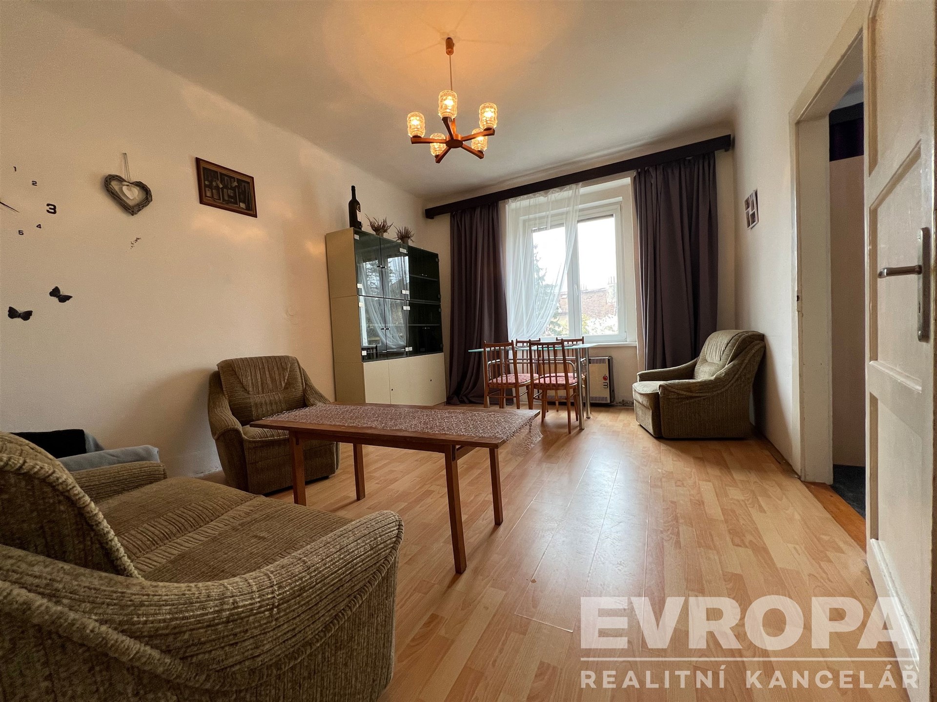 Světlý obývací pokoj s parketovou podlahou, velká okna zajišťují dostatek přirozeného světla, zařízený komfortním nábytkem, vhodný pro rodinné bydlení.