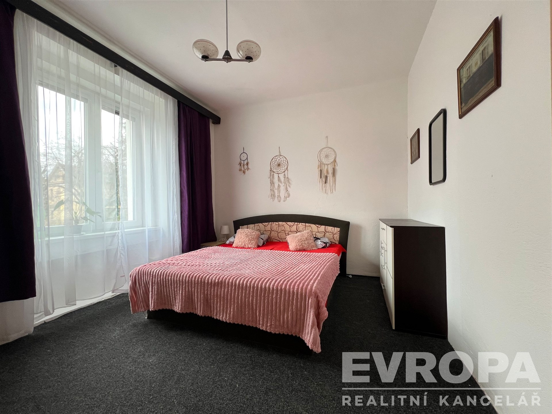 Prostorná ložnice se světlou výmalbou, velkými okny a moderní dekoračními prvky, koberec a vestavěné skříně doplňují útulný design.