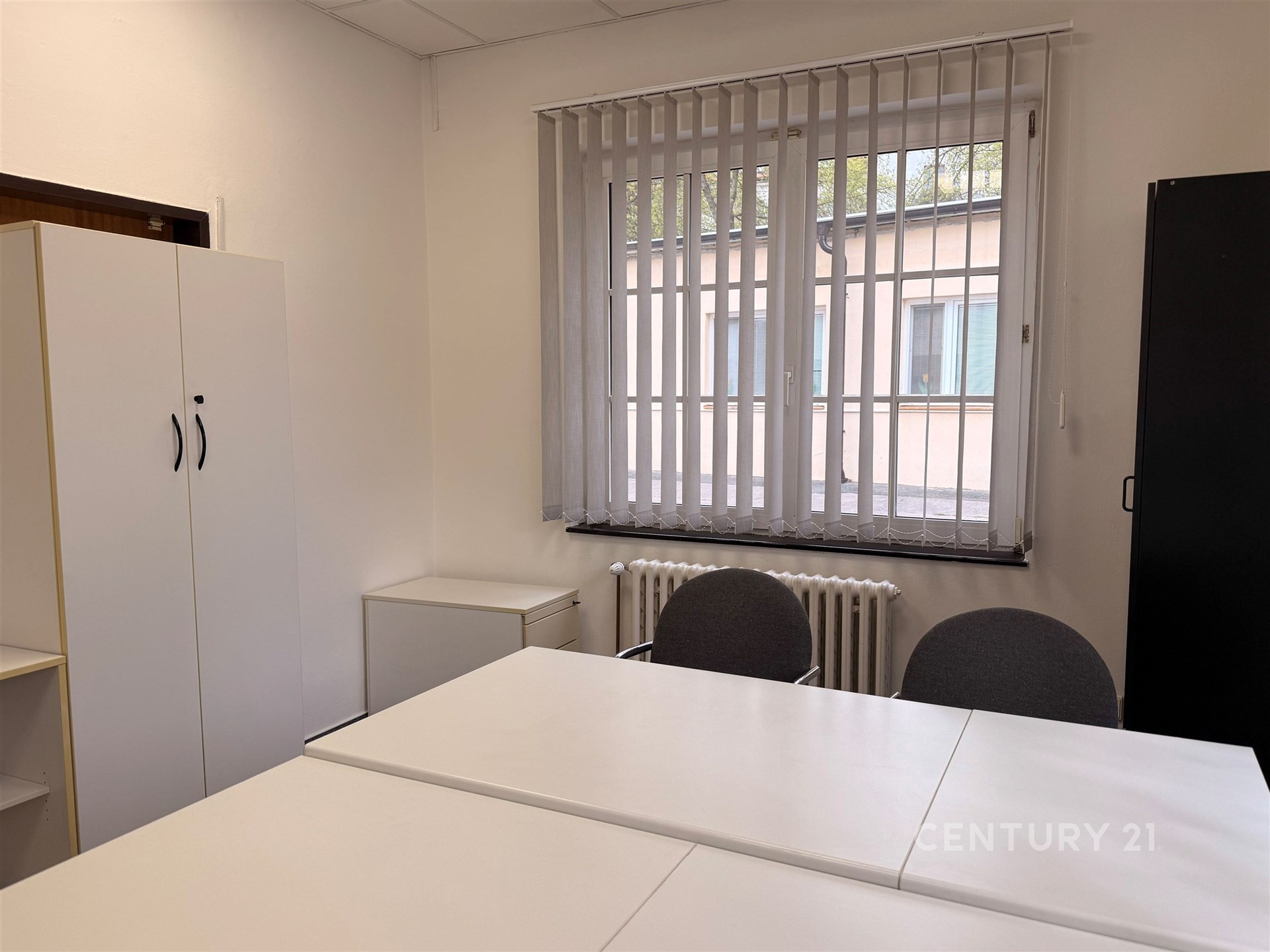 Kancelářský prostor s bílými stoly a židlemi, vestavěné skříně, velká okna se žaluziemi, moderní interiér, vhodný pro podnikání