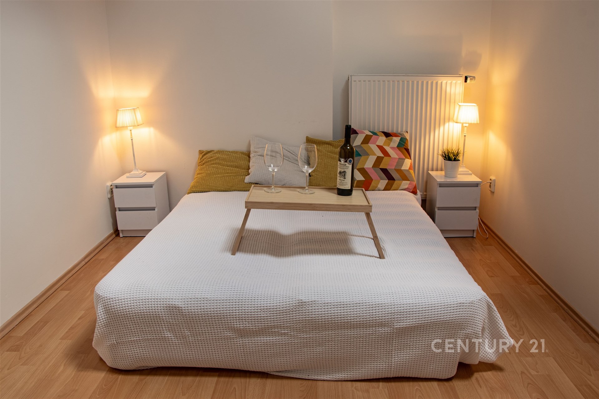 Útulná ložnice, dřevěná podlaha, moderní osvětlení, světlý styl, pohodlná postel, noční stolky, příjemná atmosféra pro relaxaci.