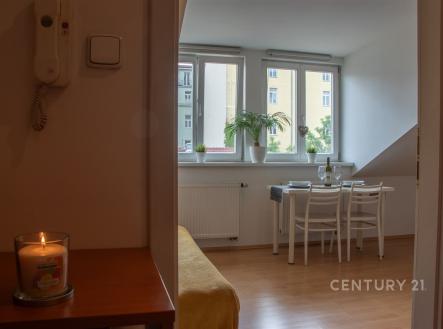 Jídelní kout s velkými okny a parketovou podlahou, moderní interiér, světlá místnost, stůl a židle.