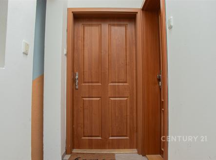 Vstupní hala s dřevěnými dveřmi, dlažbou a světlými stěnami.