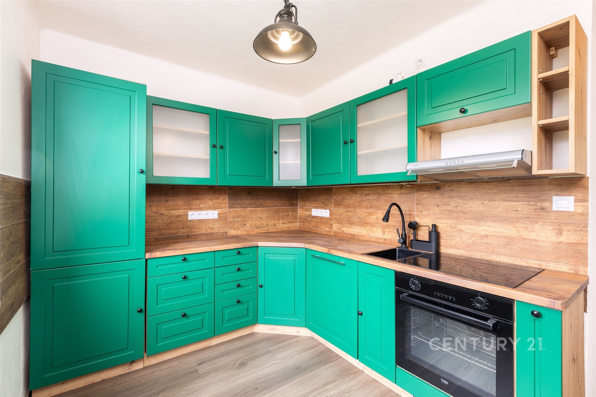 Moderní kuchyň s dřevěnou pracovní deskou, zelenými skříňkami a vestavěnou troubou. Stylový design doplňuje světlá parketová podlaha.