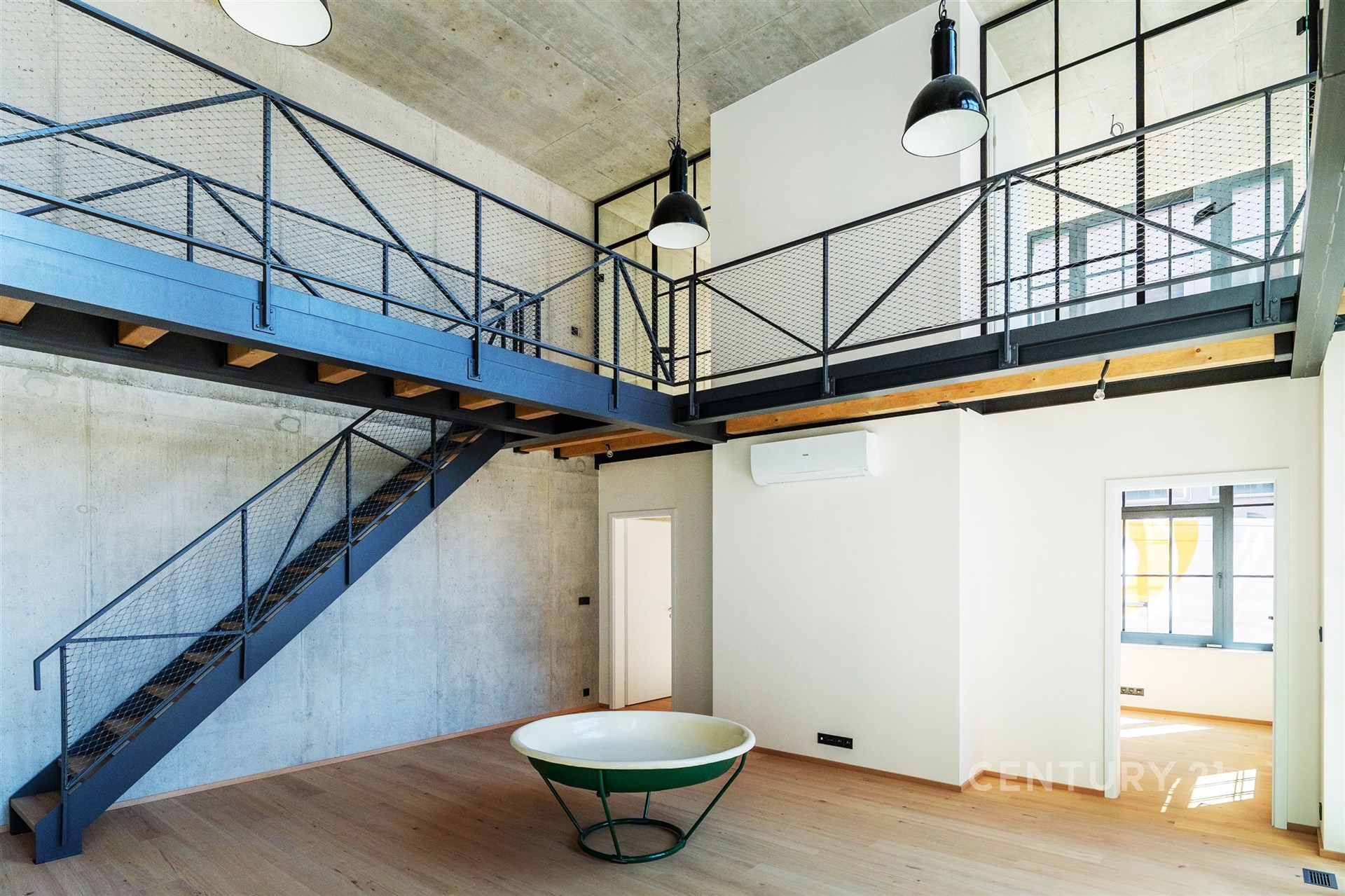 Industriální obývací pokoj s parketovou podlahou, kovovým schodištěm a vysokými stropy, moderní design a velká okna přináší světlost.