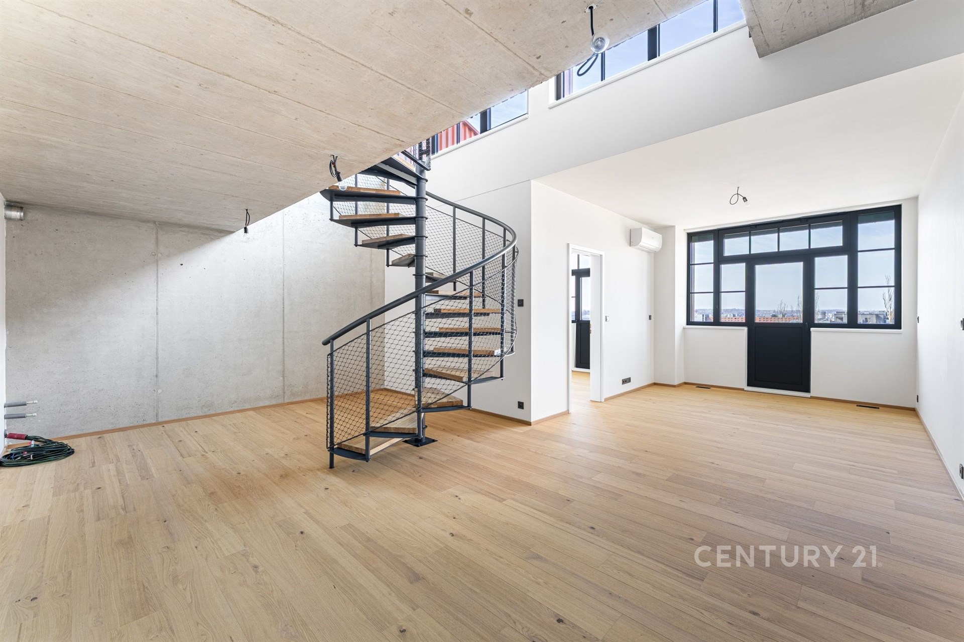 Prostorný obývací pokoj s dubovou parketovou podlahou, moderní točité schodiště a velká okna poskytující dostatek přirozeného světla