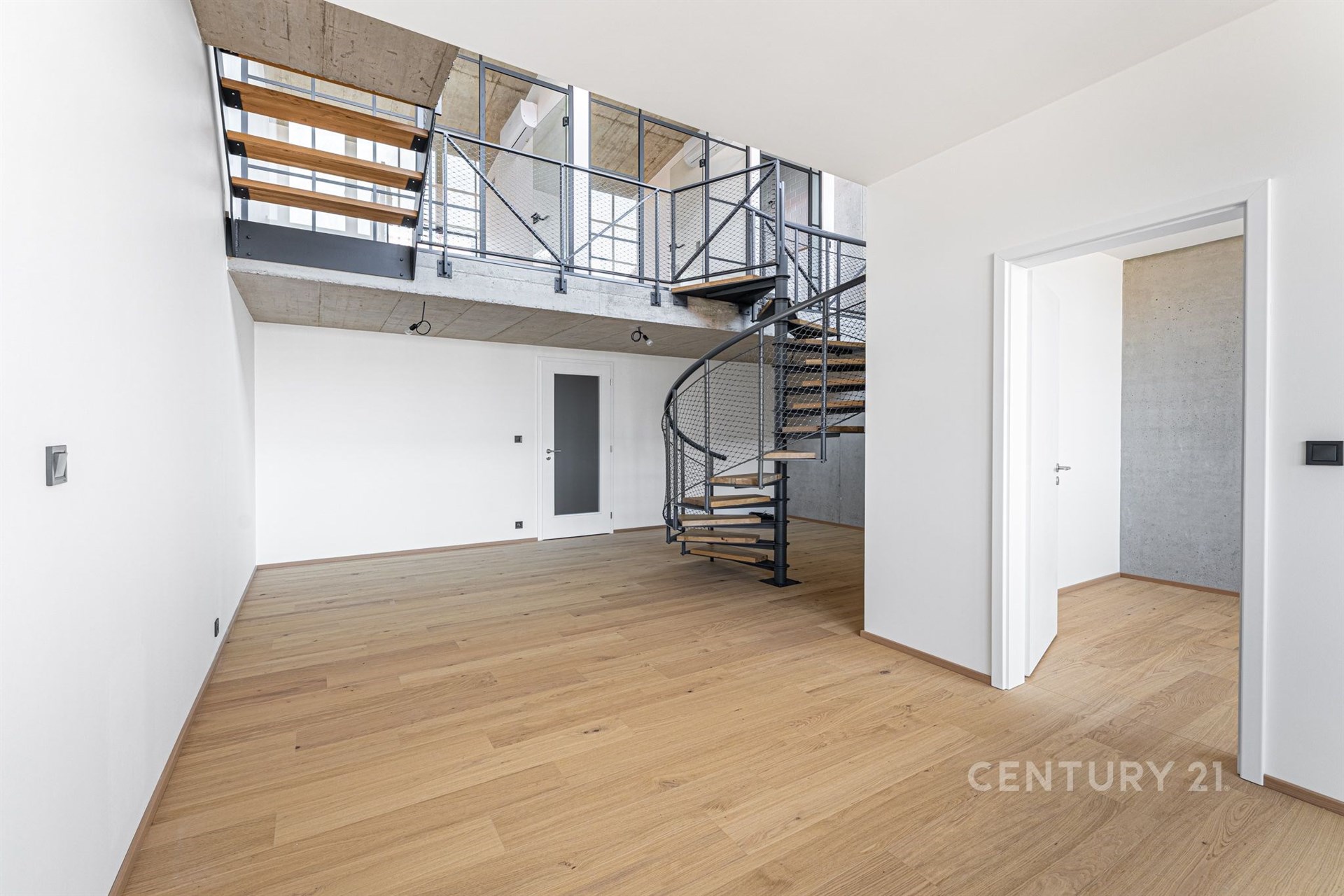 Moderní obývací prostor s parketovou podlahou, otevřeným schodištěm a vysokými stropy, který dodává prostoru světlo a vzdušnost.