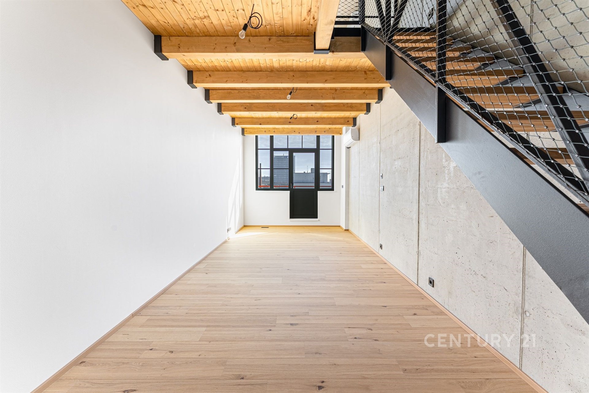 Podkrovní místnost s dřevěnými trámy, parketovou podlahou a velkými okny, moderní industriální styl, bílá stěna, betonový prvek.
