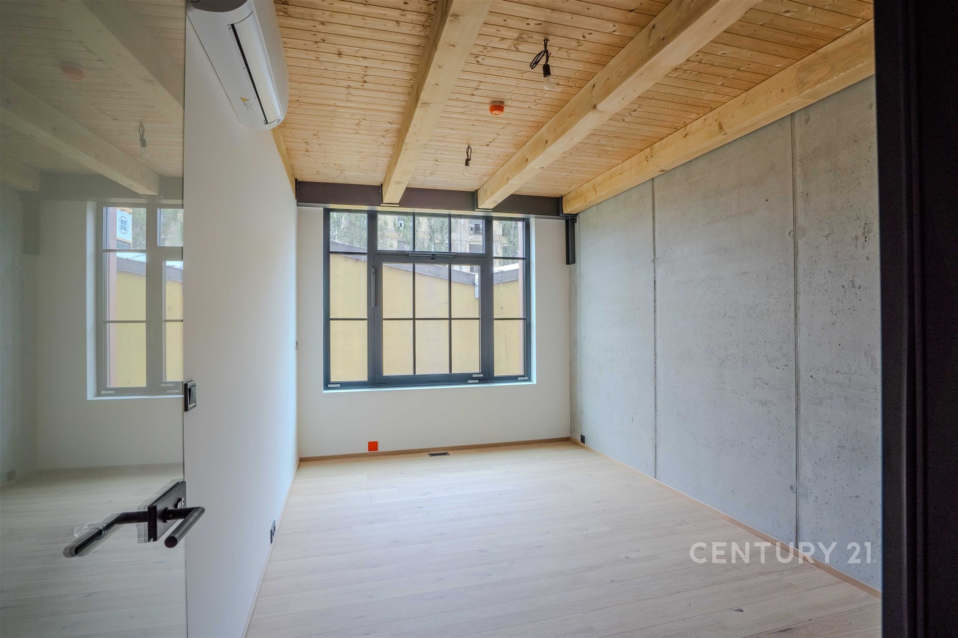 Prázdná místnost s velkými okny, dřevěným stropem a parketovou podlahou, moderní styl a přirozené osvětlení.