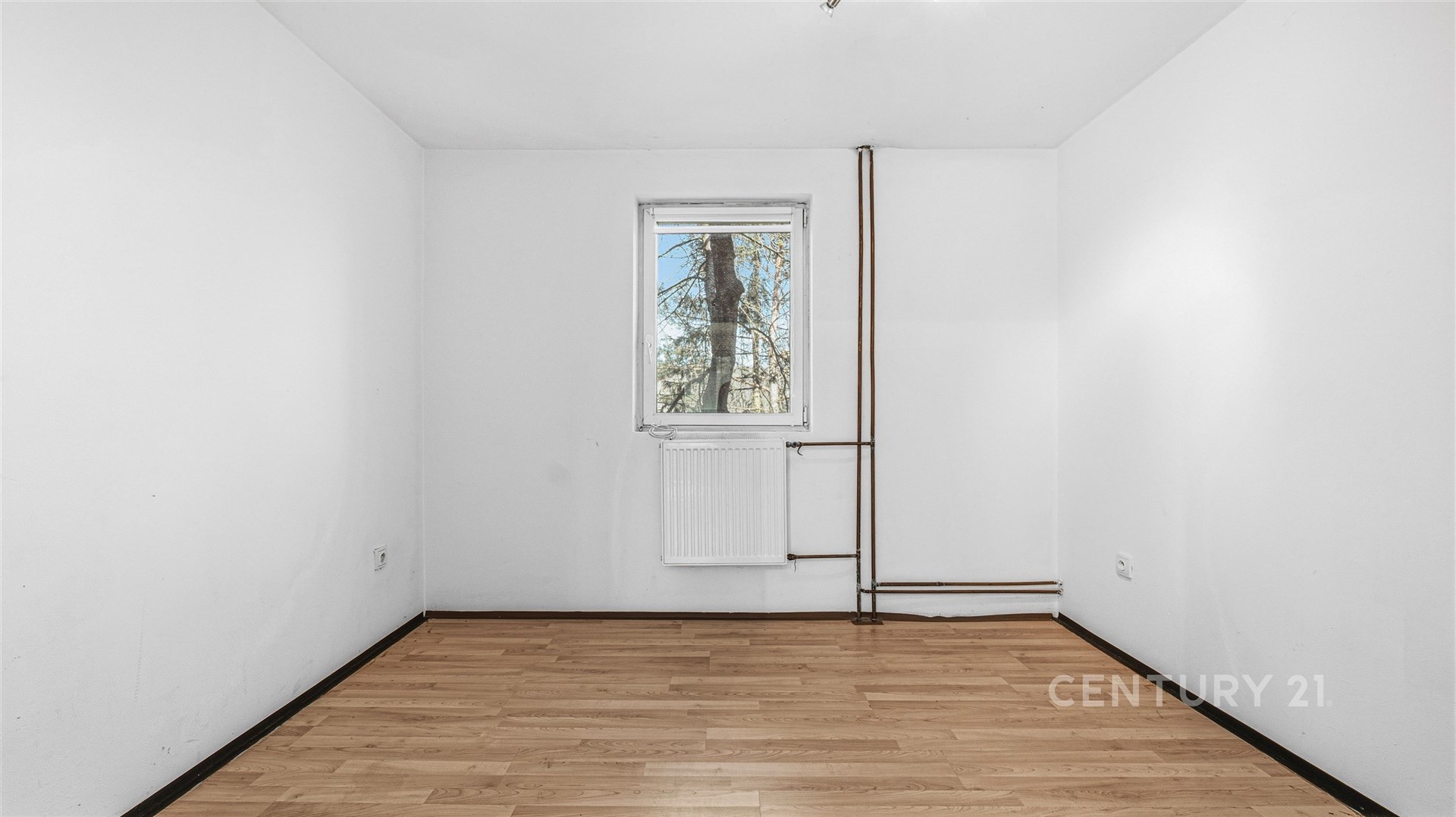 Prázdný pokoj s parketovou podlahou, bílými stěnami a oknem s výhledem na přírodu, vhodný pro rekonstrukci a vlastní designové úpravy.