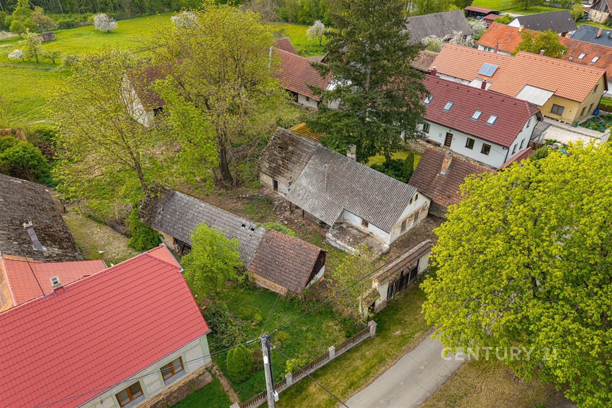 Venkovský pozemek se starými budovami, červená střecha, okolní zeleň, klidná lokalita. Potenciál pro rekonstrukci či nový výstavbu.
