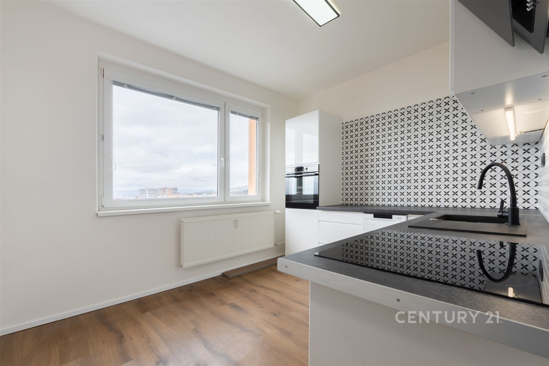 Moderní kuchyň s parketovou podlahou, velkým oknem a černobílými obklady. Světlý prostor s vestavěnými spotřebiči.