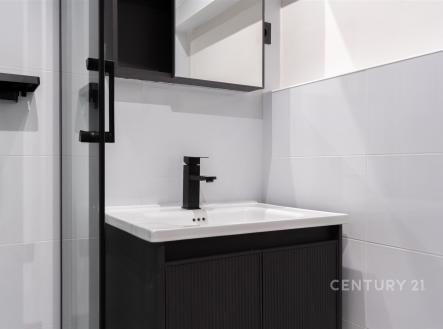 Moderní koupelna s černými doplňky, elegantní dlažbou a kvalitním sprchovým koutem vytváří funkční a stylový prostor.