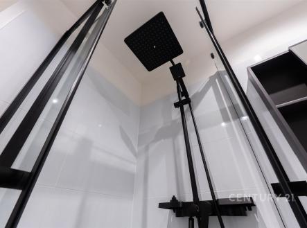 Moderní sprchový kout s černými skleněnými dveřmi, elegantním dešťovým sprchovým panelem a světlými keramickými obklady