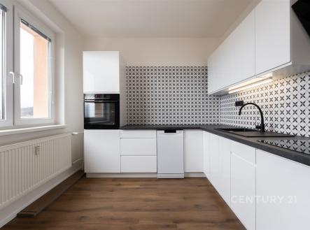 Moderní kuchyň s parketovou podlahou, světlými bílými skříňkami a stylovým keramickým obkladem. Velká okna zajišťují dostatek světla.