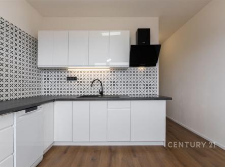 Moderní kuchyň, bílá lesklá dvířka, parketová podlaha, elegantní dlažba, světlý prostor.