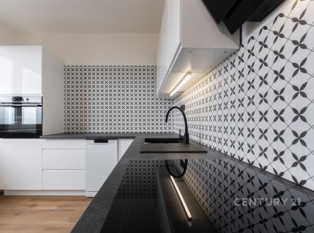 Moderní kuchyň s černobílou dlažbou, vestavěnými spotřebiči a parketovou podlahou, nabízí elegantní a funkční design.